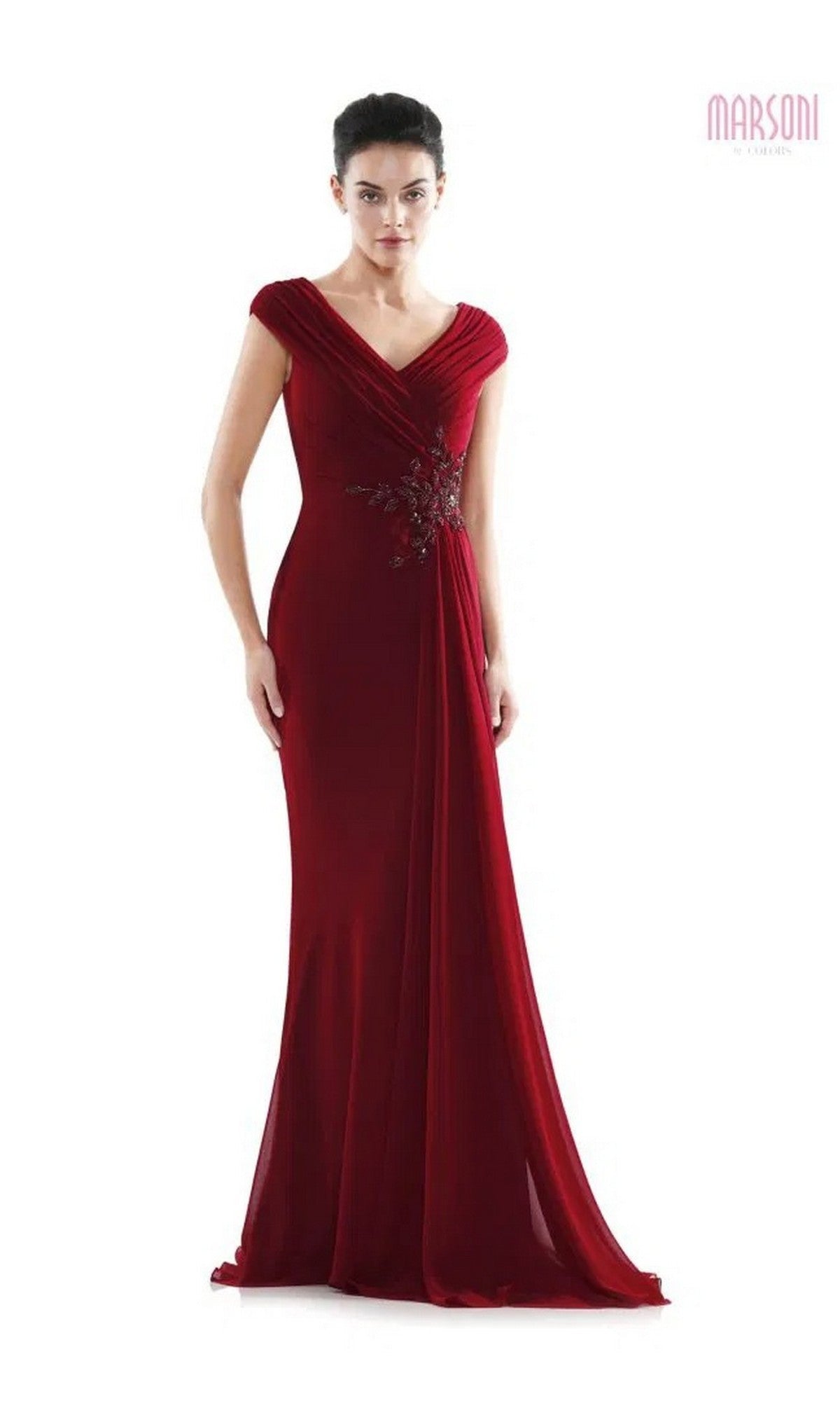 A woman stands against a plain white background wearing the Marsoni MV1080 long formal dress in wine, featuring a floor-length chiffon design with a v-neckline, cap sleeves, and floral embellishment at the waist.